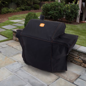 Black grill cover protects a barbecue. It has a red trim. The cover is on a patio.