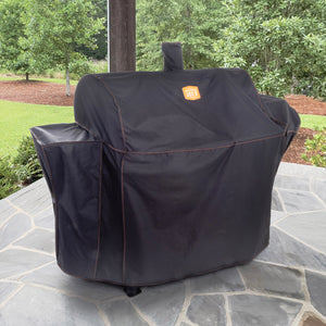 Black Weber grill cover protects a barbecue. It sits on a stone patio.