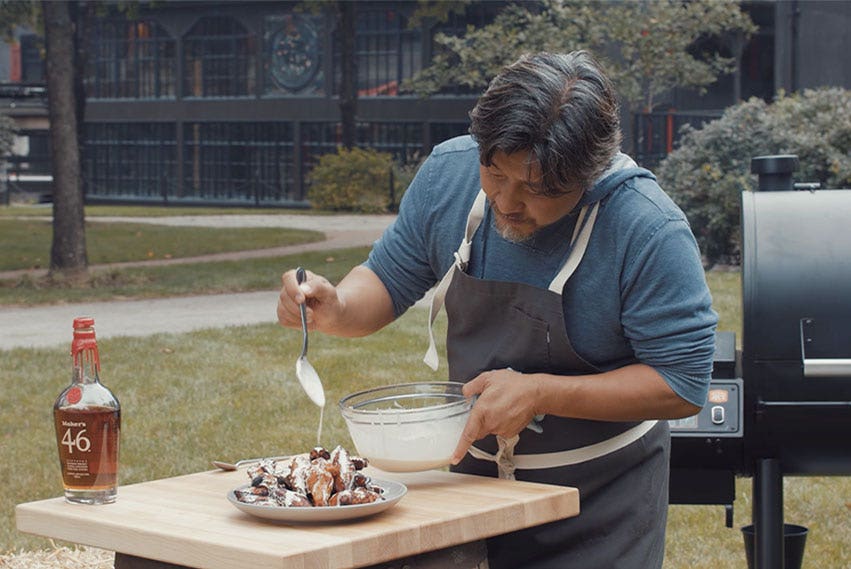 Chef Edward Lee drizzling sauce from a spoon onto a plate of chicken wings.